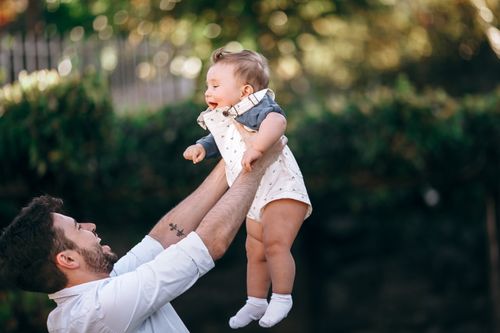 Free A joyful outdoor moment of a father lifting his smiling baby, captured in warm natural light. Stock Photo