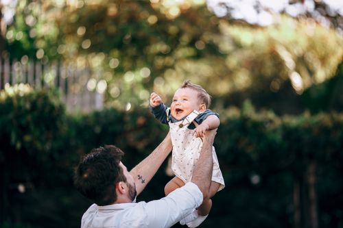 Free A joyful father plays with his baby outdoors on a sunny summer day, capturing a beautiful family moment. Stock Photo