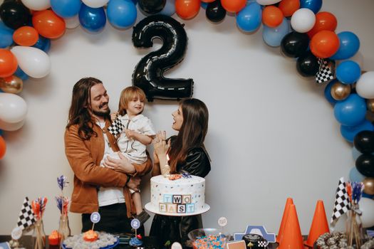 Joyful family celebrating a 2-year-old's birthday with a race car theme and colorful balloons.