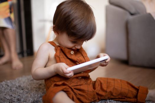 Cute toddler in a brown outfit enjoying a tablet indoors. Perfect stock image for technology or family content.