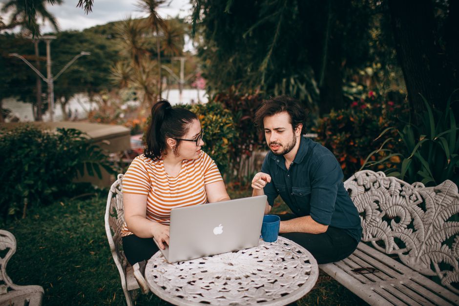 A man and woman working together on a laptop outdoors in a lush garden