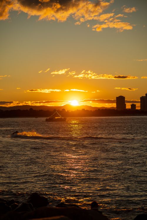 Free A serene ocean sunset with a silhouetted boat and skyline, capturing tranquil seascape colors. Stock Photo