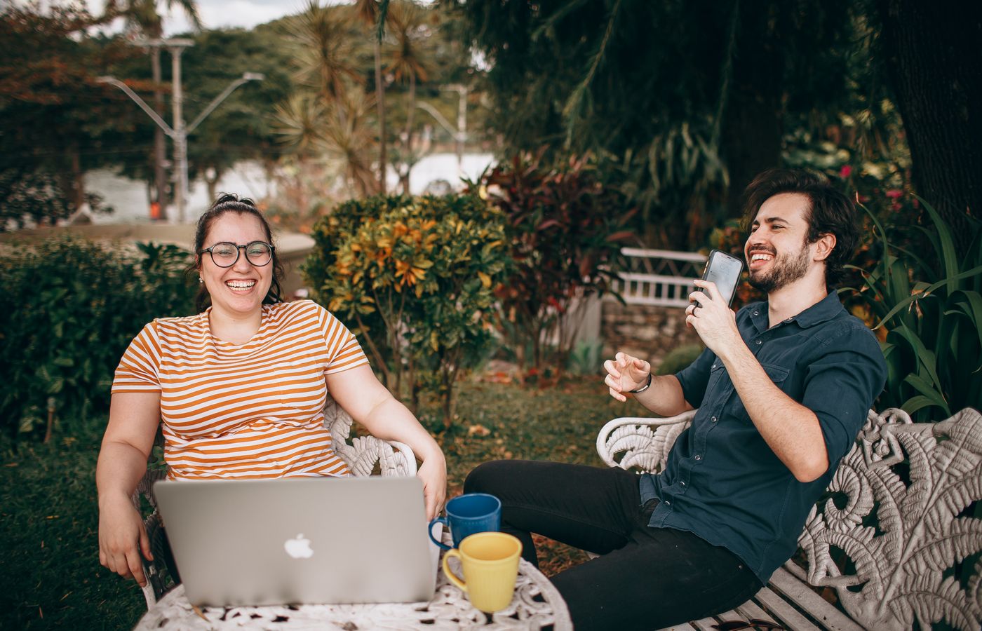 Two happy friends taking a break outdoors with a laptop and a smartphone.