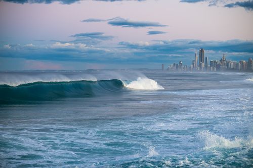 Free A tranquil coastal scene with waves and a distant city skyline under a colorful sky. Stock Photo
