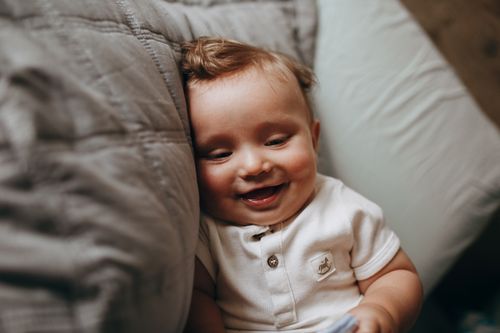 Free Close-up of a happy baby smiling while lying on a soft surface indoors. Stock Photo
