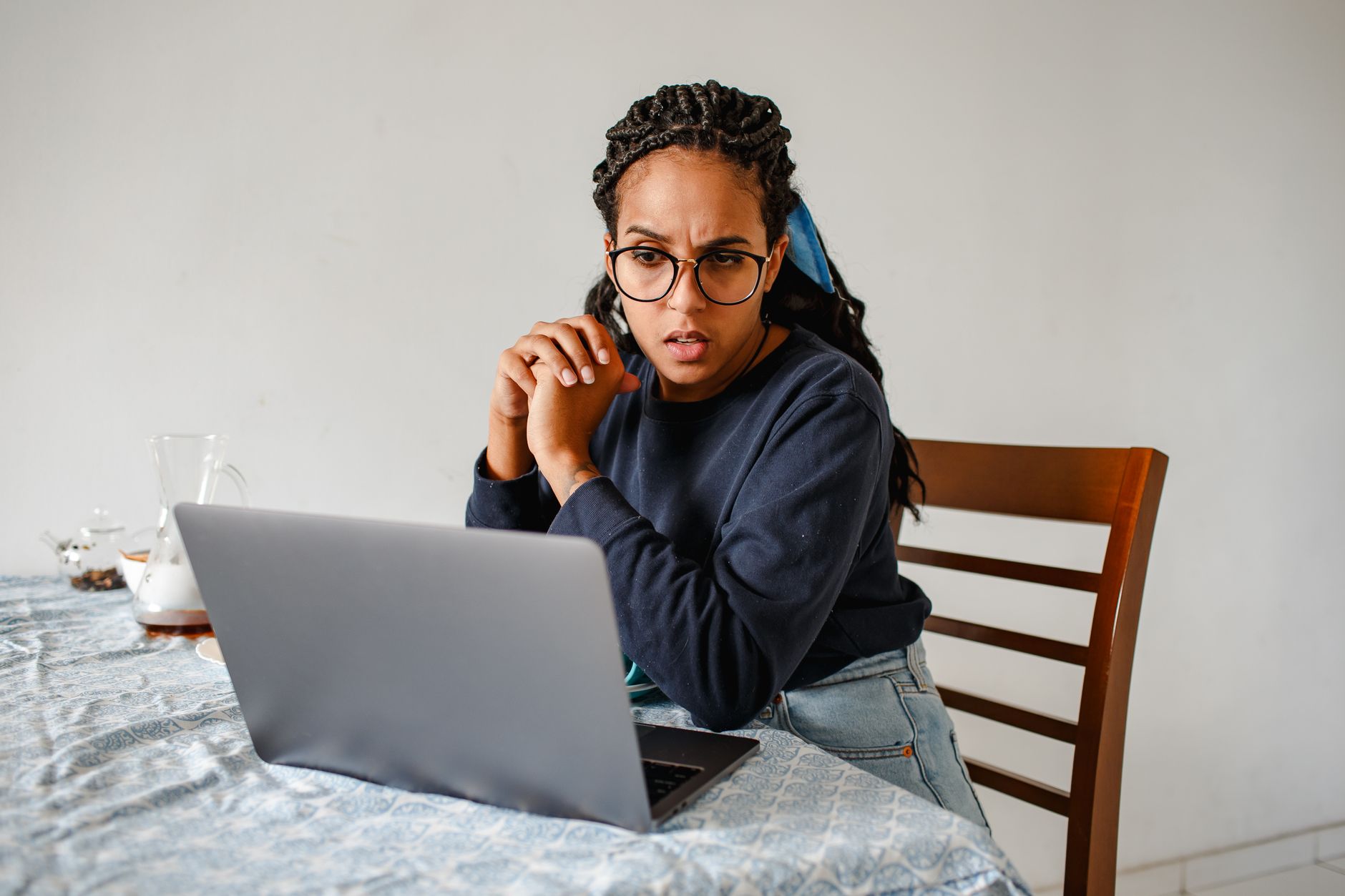 Woman intently working on a laptop, seated at a table in a cozy home environment.