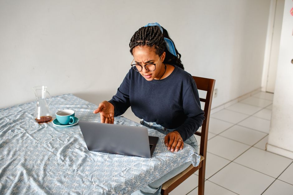 How to Find Motivation to Write My Essay: 7 Proven Strategies 2 A frustrated woman using a laptop with coffee at a home table, expressing concern.