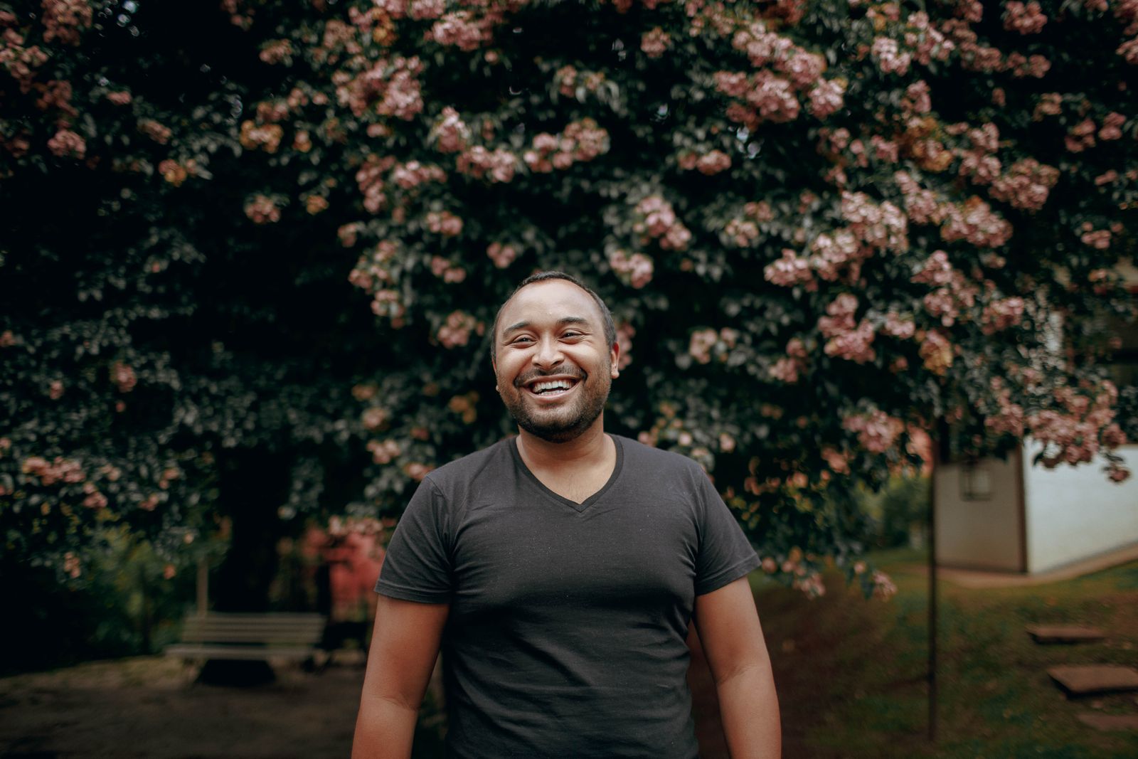 A laughing man in a dark T-shirt standing in front of a tree covered in pink blossom