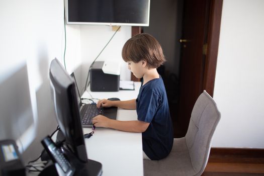A young boy focuses intently while using a computer at his home desk.