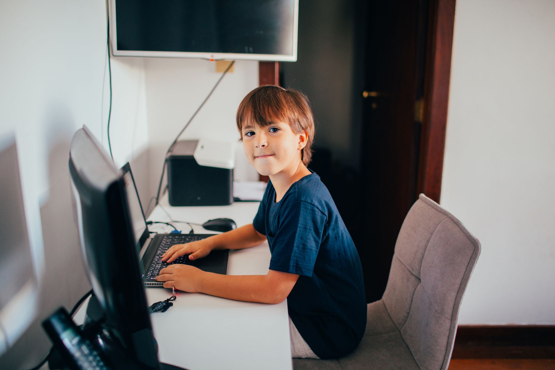 A young boy sitting at a desk using a computer at home, fostering digital learning.