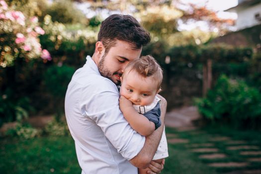 Emotional moment of a father holding his baby outdoors in a sunny garden.
