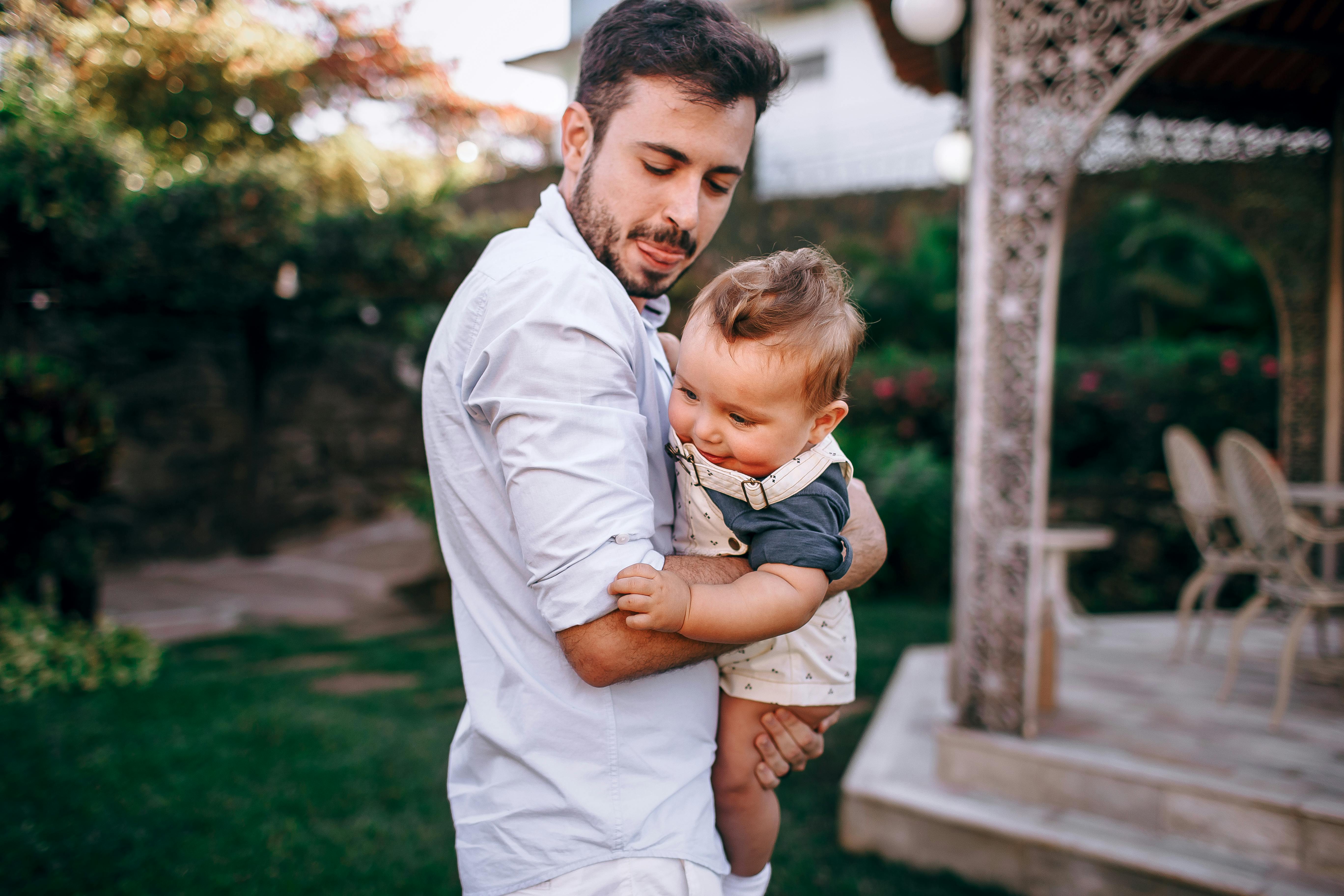 A father lovingly holds his baby in an elegant garden setting, showcasing tender family warmth.