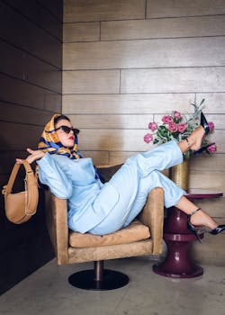 Fashionable woman in blue outfit and headscarf lounging in a modern indoor setting with flowers.