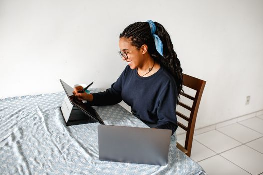 Woman working remotely using a tablet and laptop at home. Ideal for tech or remote work themes.