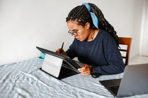Free Young woman concentrating on digital art using a tablet indoors, showcasing focus and technology. Stock Photo