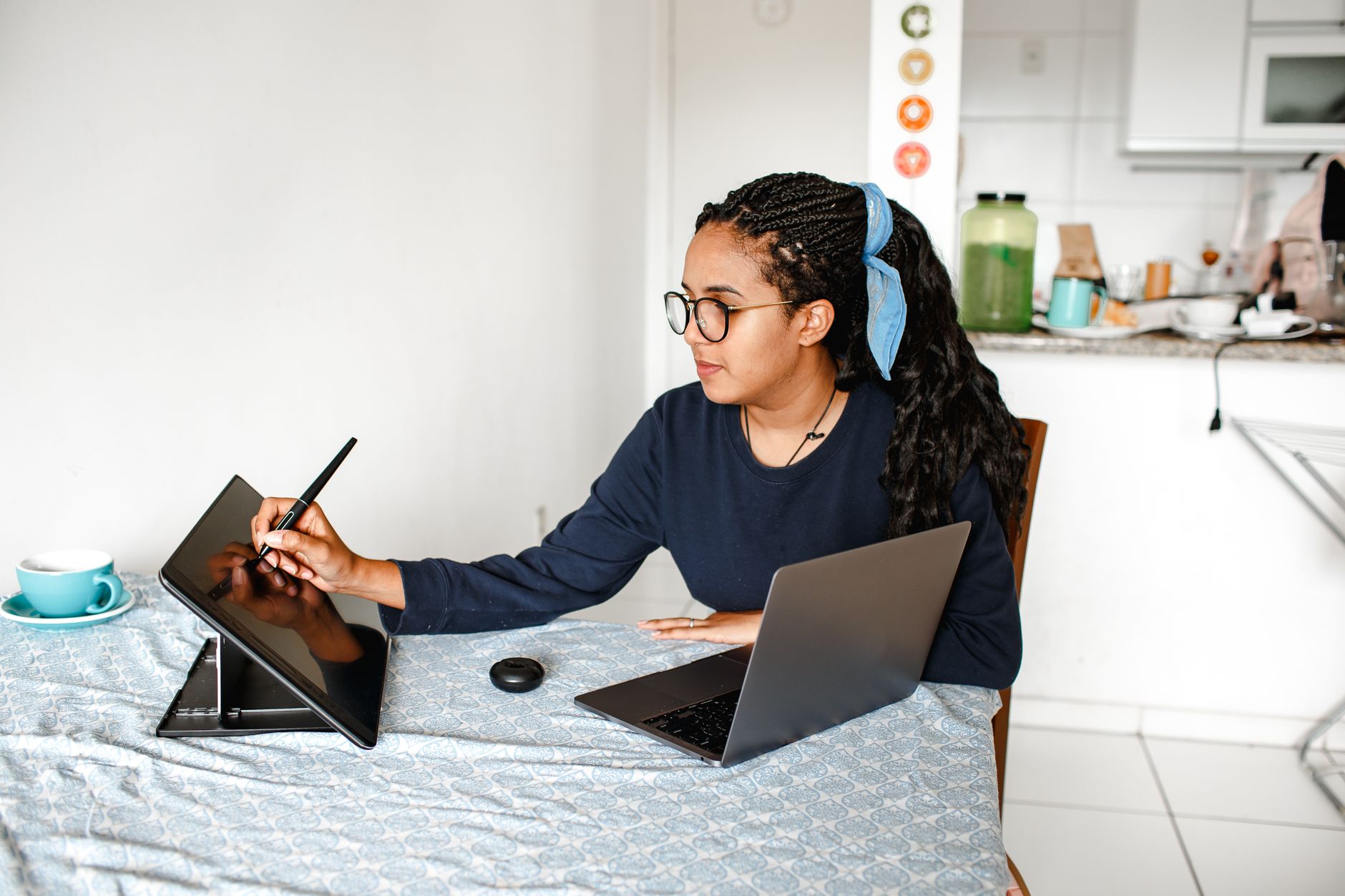 Young woman using digital tablet and laptop at home, focused on creative work.