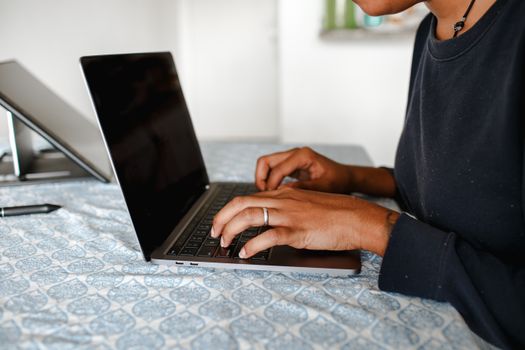 Close-up of an adult typing on a laptop in a cozy indoor setting.