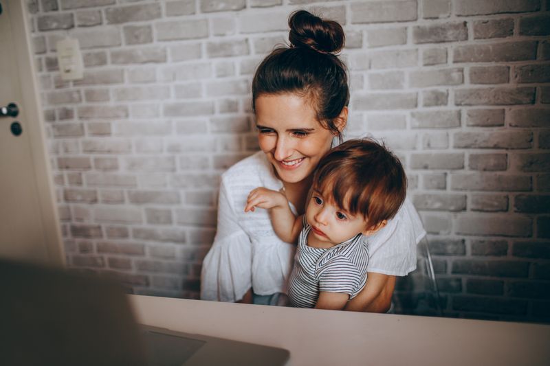 A colleague working at a laptop with her child on her lap, photo by Helena Lopes on Pexels