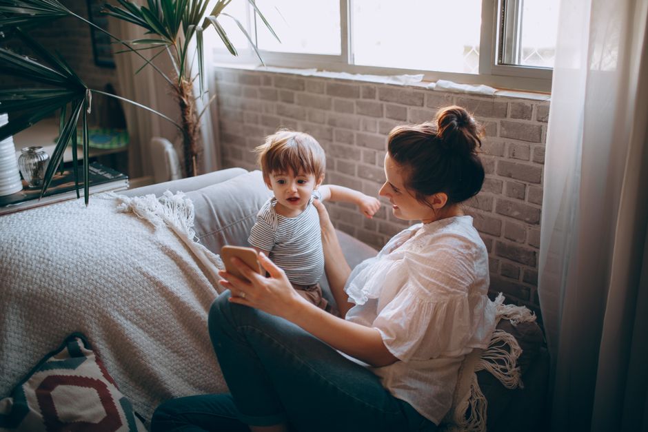 A mother and child bonding on the sofa, enjoying time together with a smartphone in a cozy home setting.