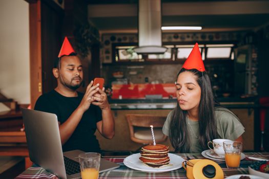 Two adults celebrate a birthday indoors, wearing party hats with a pancake cake.