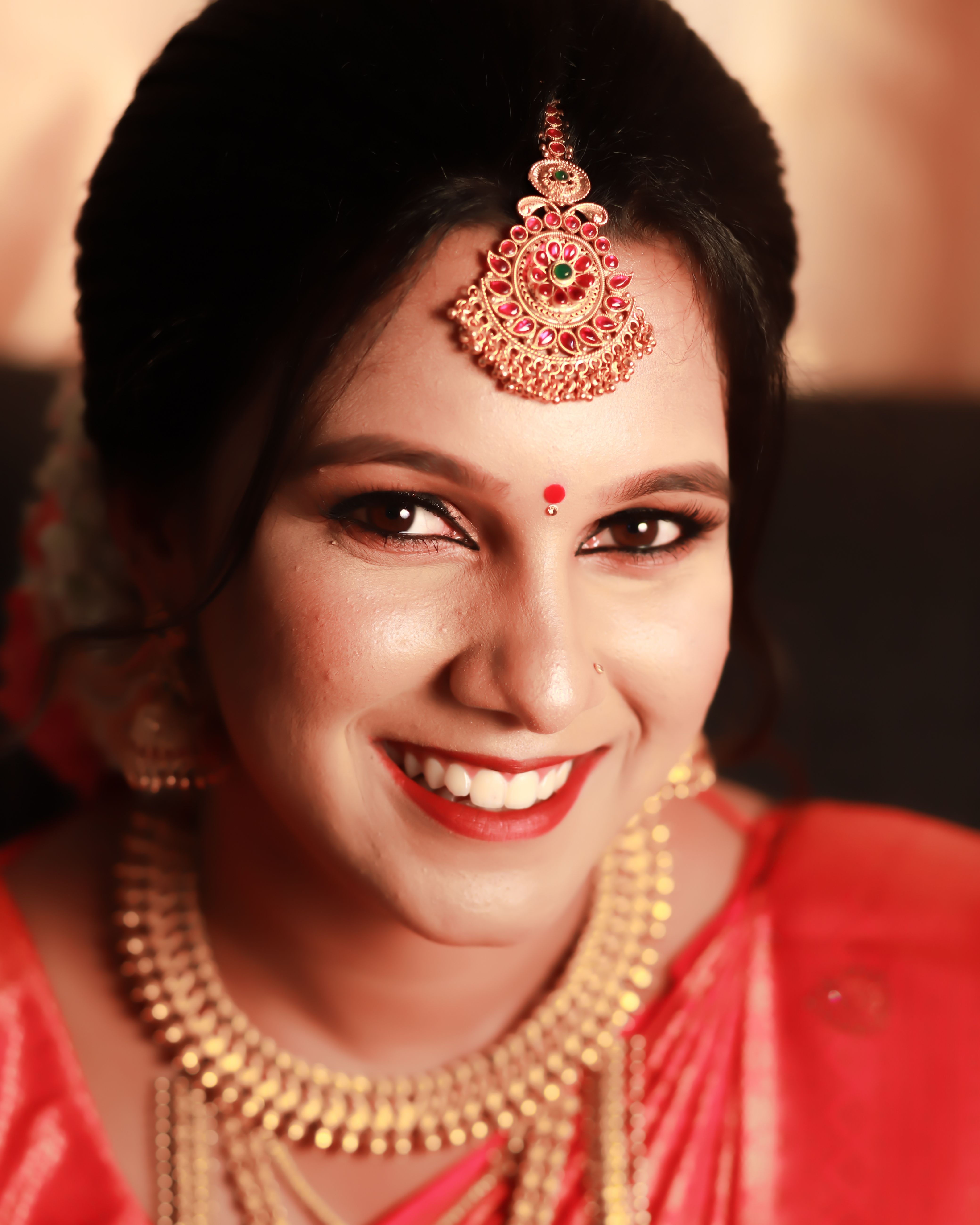 Smiling South Indian bride in traditional attire with intricate jewelry, photographed in warm tones.