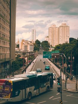 Vibrant city street with bus, cars, and towering skyscrapers under a cloudy sky.