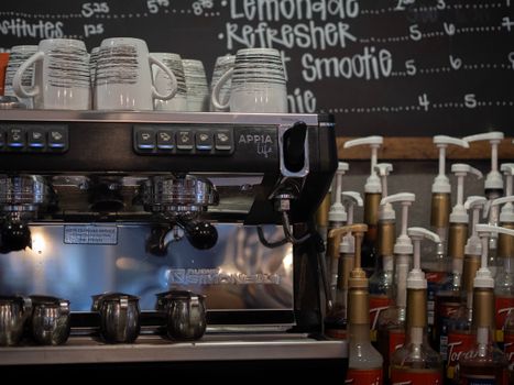 Close-up of a Nuova Simonelli espresso machine with coffee cups and syrup bottles in a cozy café.