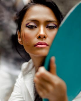 A focused close-up of a woman applying makeup using a compact mirror outdoors.