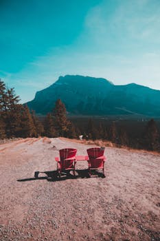 Two red Adirondack chairs overlooking a mountain in Banff National Park, Alberta, Canada during a clear day.