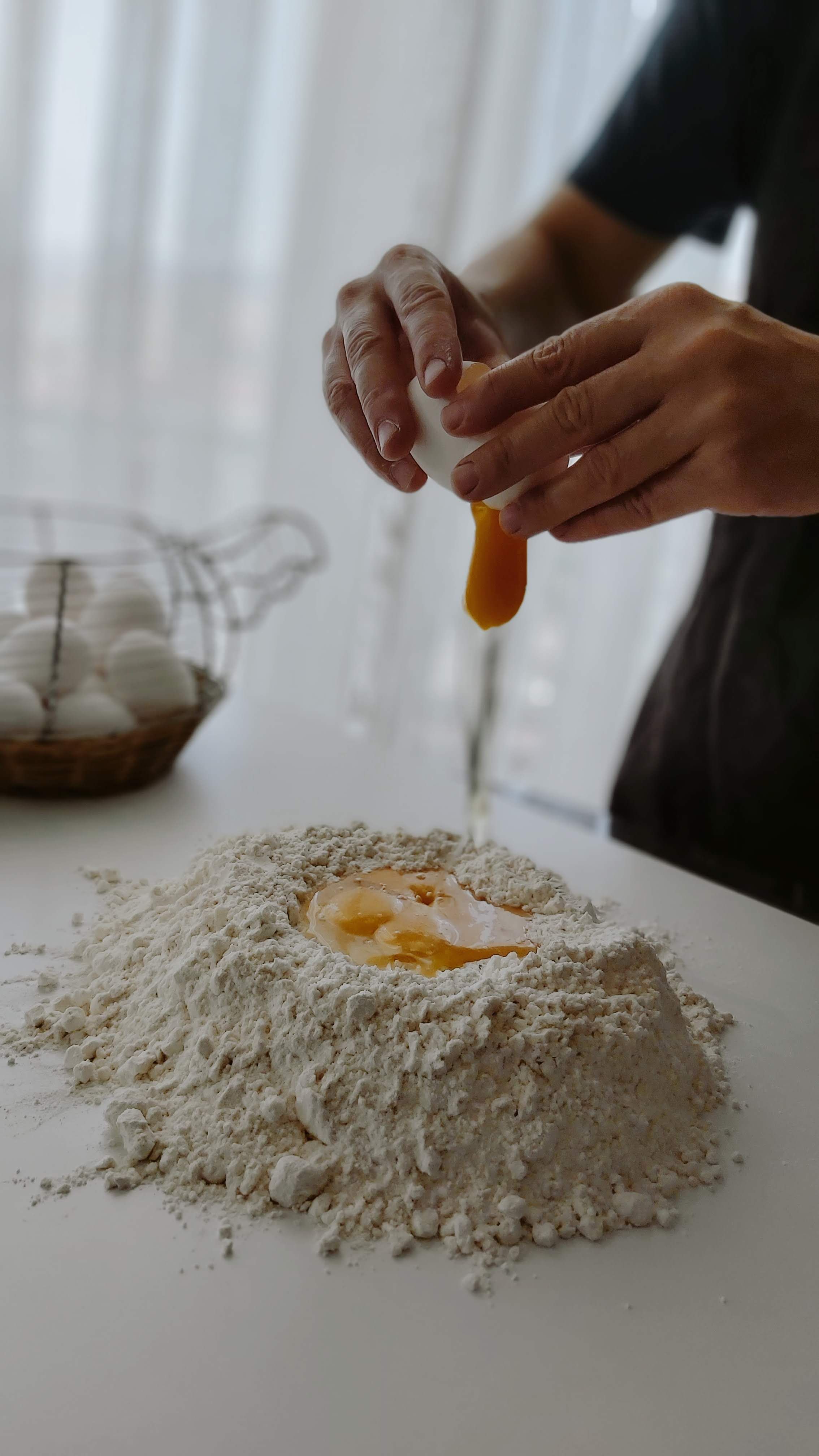 Hands breaking eggs into flour for dough preparation, indoors and homemade.