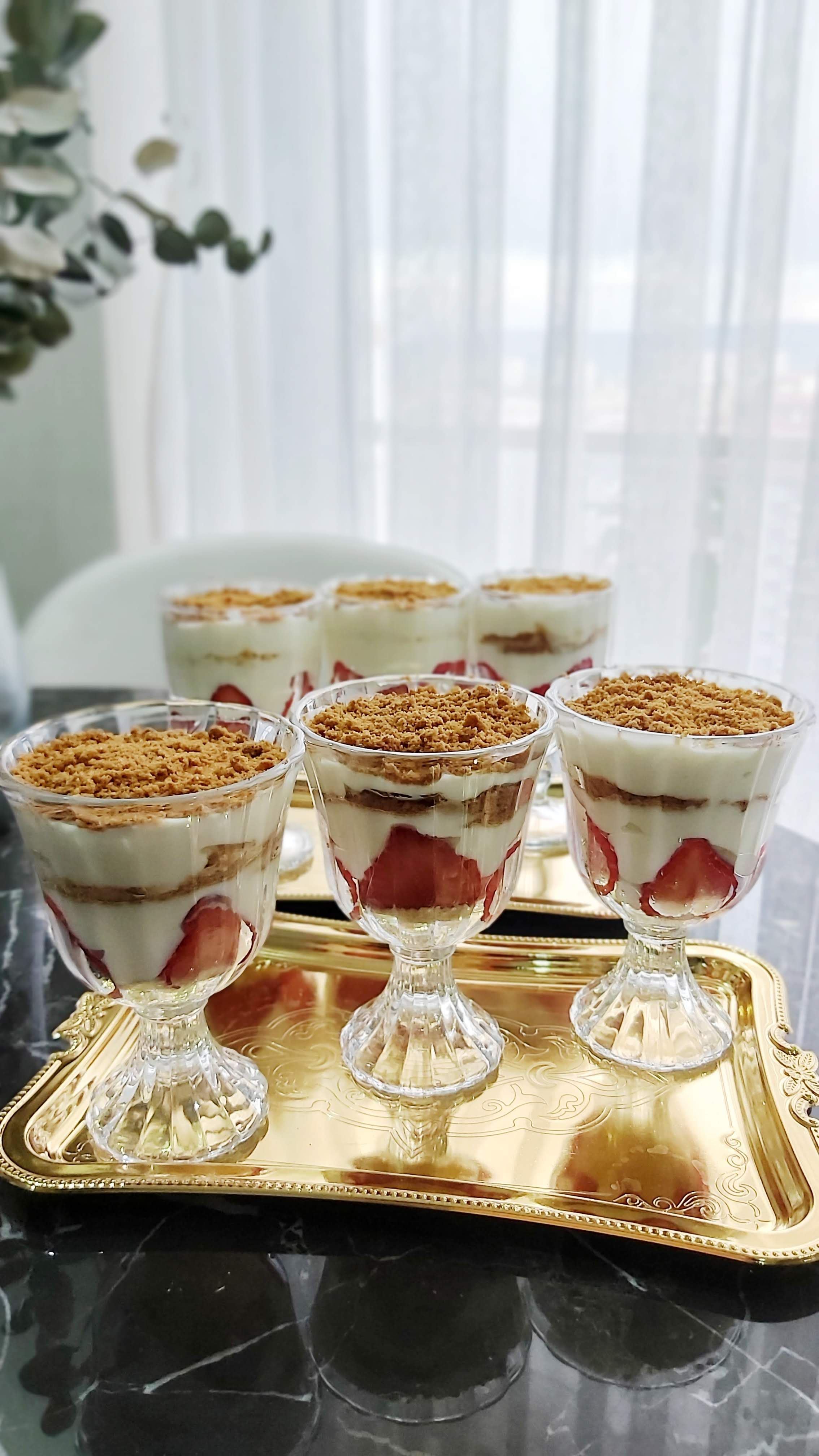 Glass parfaits layered with yogurt, strawberries, and granola on a gold tray.