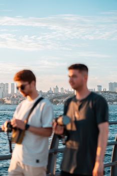 Two men on a waterfront overlook the city skyline during a sunny day.