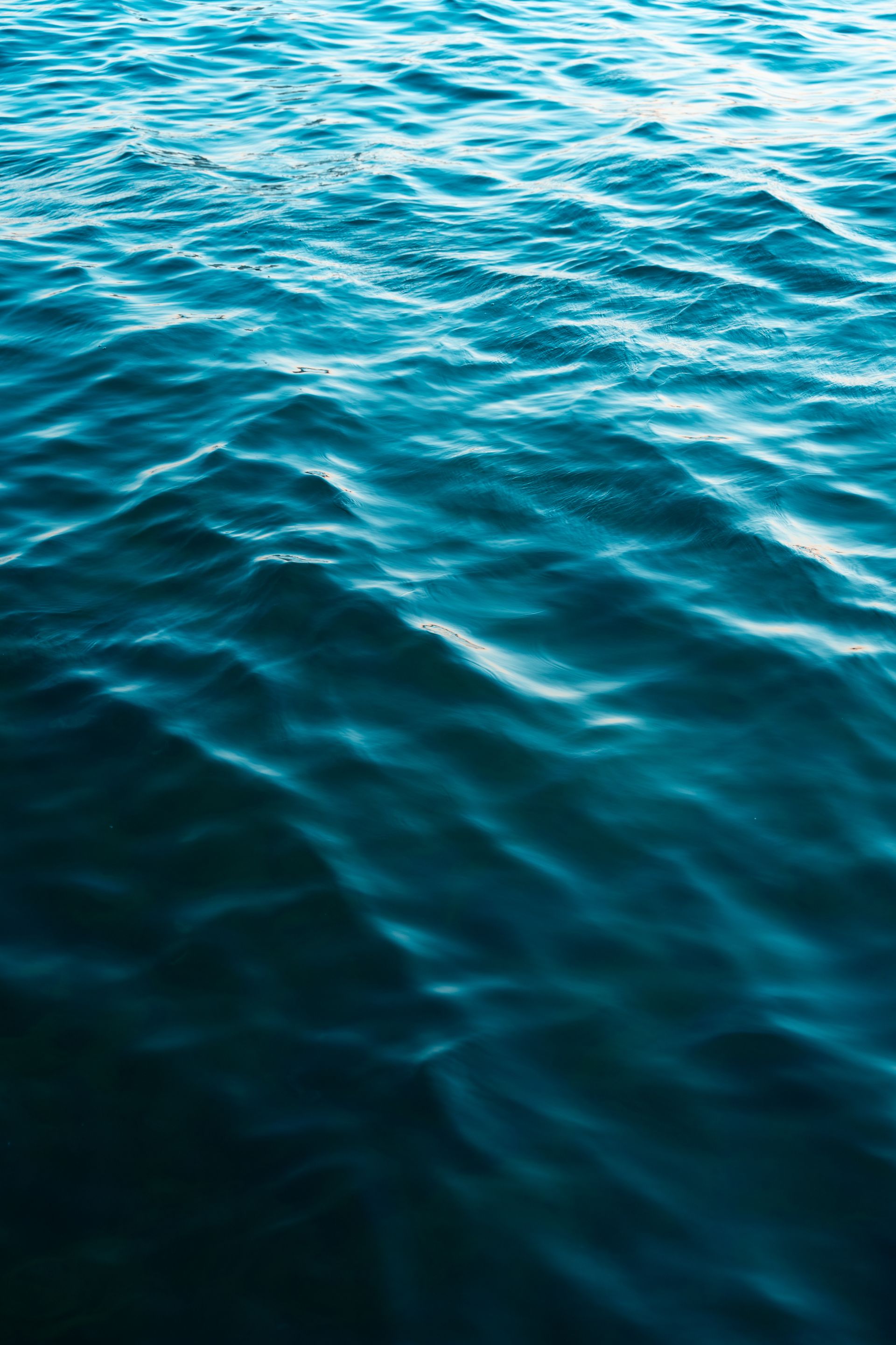 Vibrant turquoise ocean waves creating abstract ripple patterns on a sunny day.