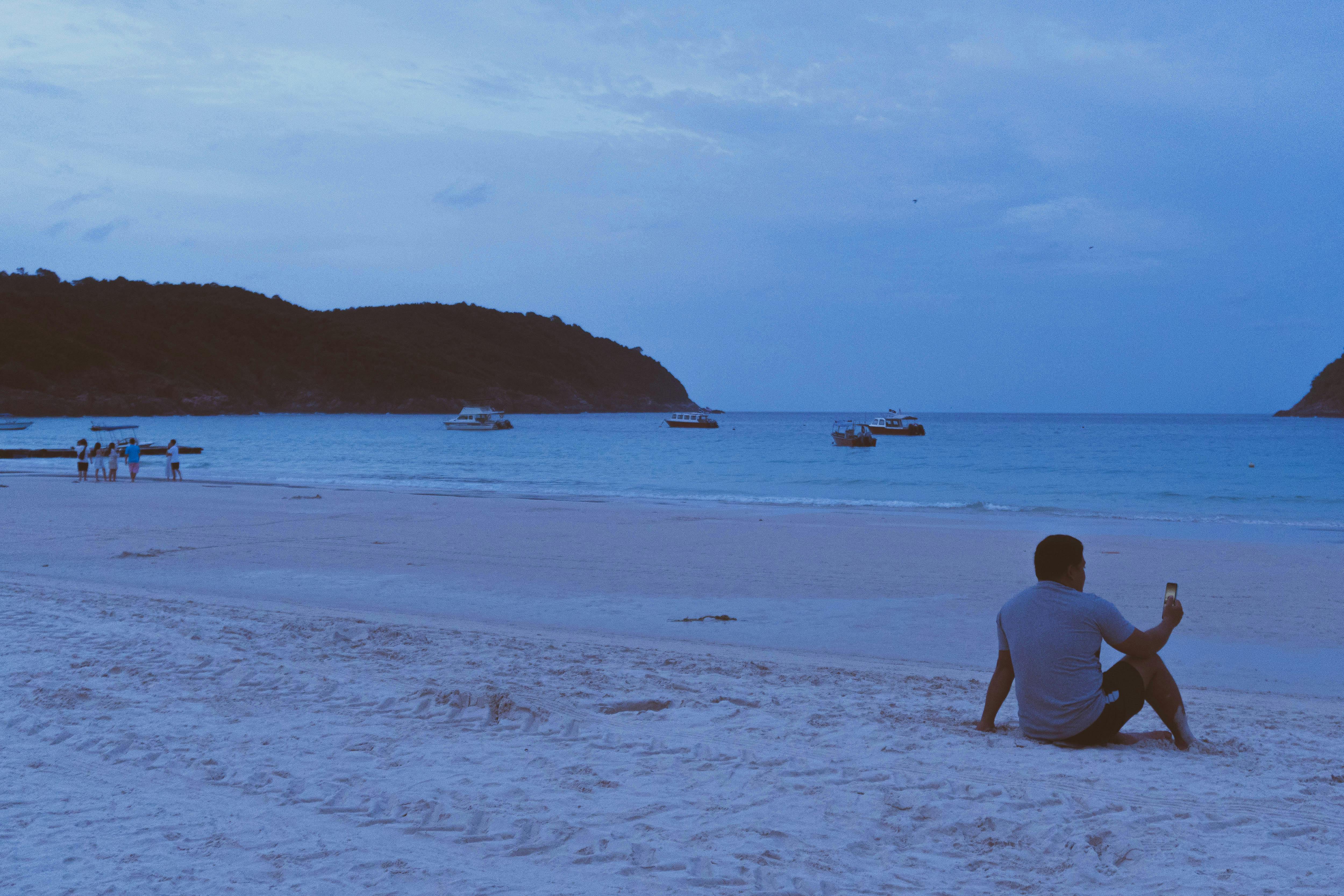 blue toned image of a man sitting on a sandy beach