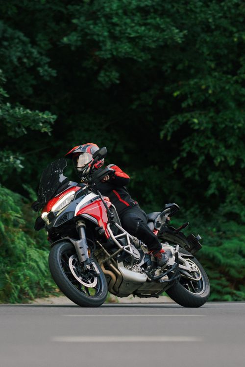 Free Motorcyclist wearing helmet rides on a red motorcycle along a forested road, showcasing dynamic motion. Stock Photo
