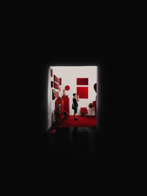 A person stands in a modern red-themed interior viewed from a dark shadowy hallway.