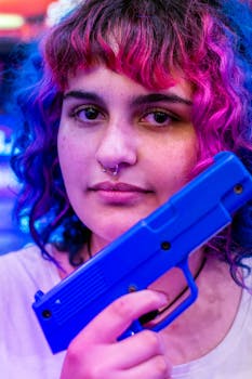 照片特写中，一名女子手持蓝色玩具枪，头发颜色鲜艳