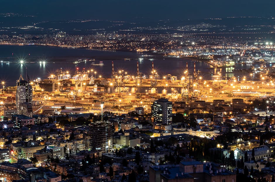 Aerial view of a bustling port city at night with illuminated buildings and harbor lights.