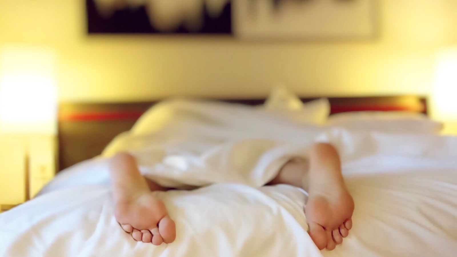 A person resting beneath white bedding in a softly lit room