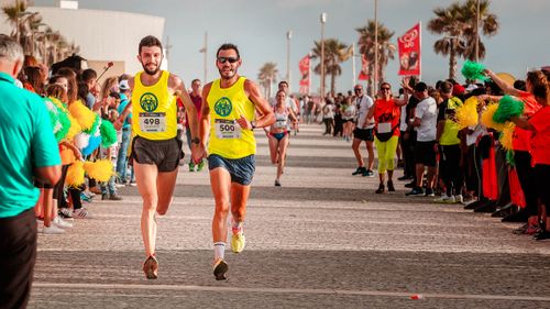 Free Two runners in a city marathon surrounded by cheering fans and vibrant atmosphere. Stock Photo