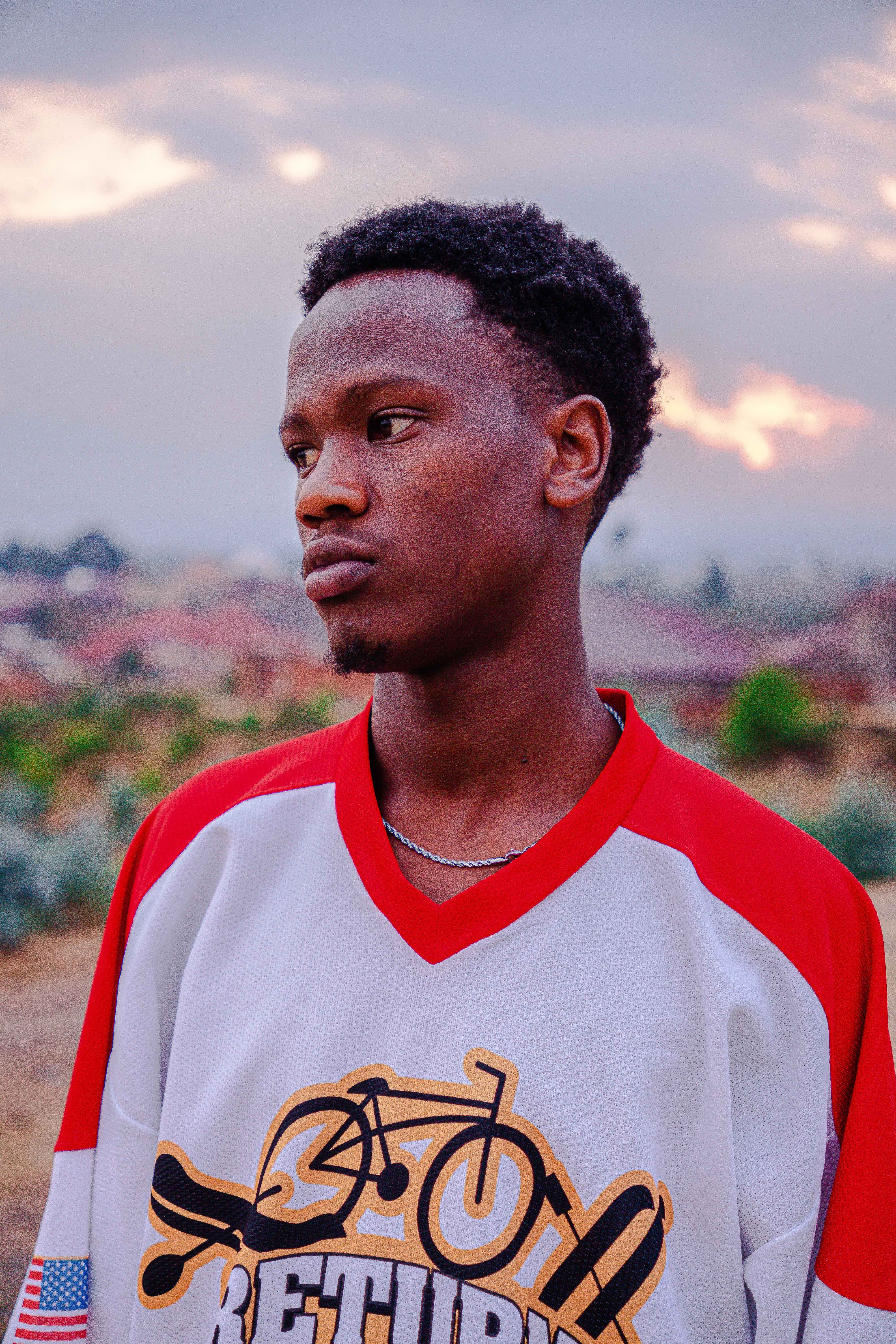 Portrait of a thoughtful young man in a sports jersey outdoors during sunset.