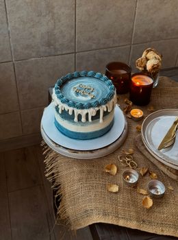 Elegant blue birthday cake displayed with candles on a rustic table setting.
