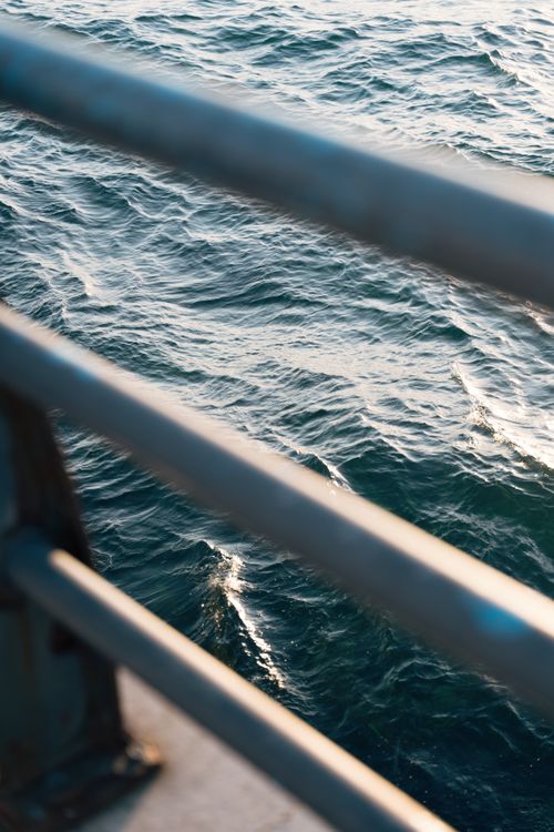 Free A view of the ocean with sunlight reflections, seen through a pier railing. Stock Photo