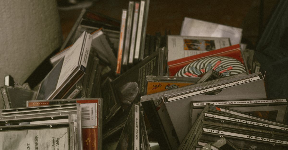 A vintage car stereo and a stack of burned CDs with handwritten sharpie labels on the passenger seat