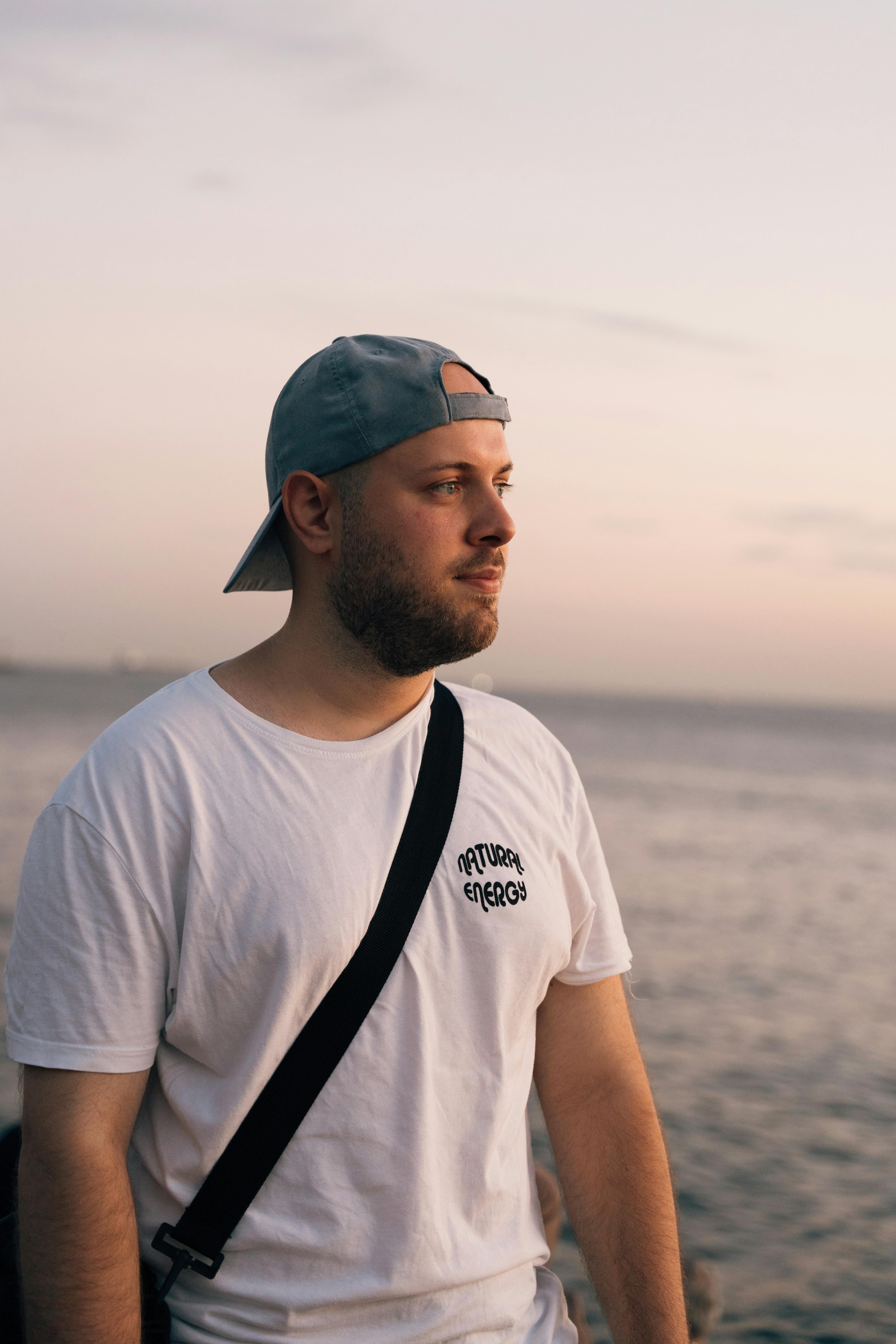 a man with a hat and backpack standing by the ocean