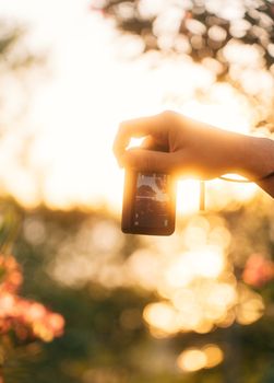 A hand holding a smartphone captures a vibrant summer sunset outdoors