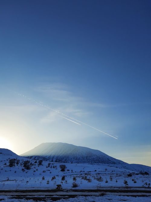 Free A serene winter landscape with a snow-capped mountain under a clear blue sky at sunrise. Stock Photo