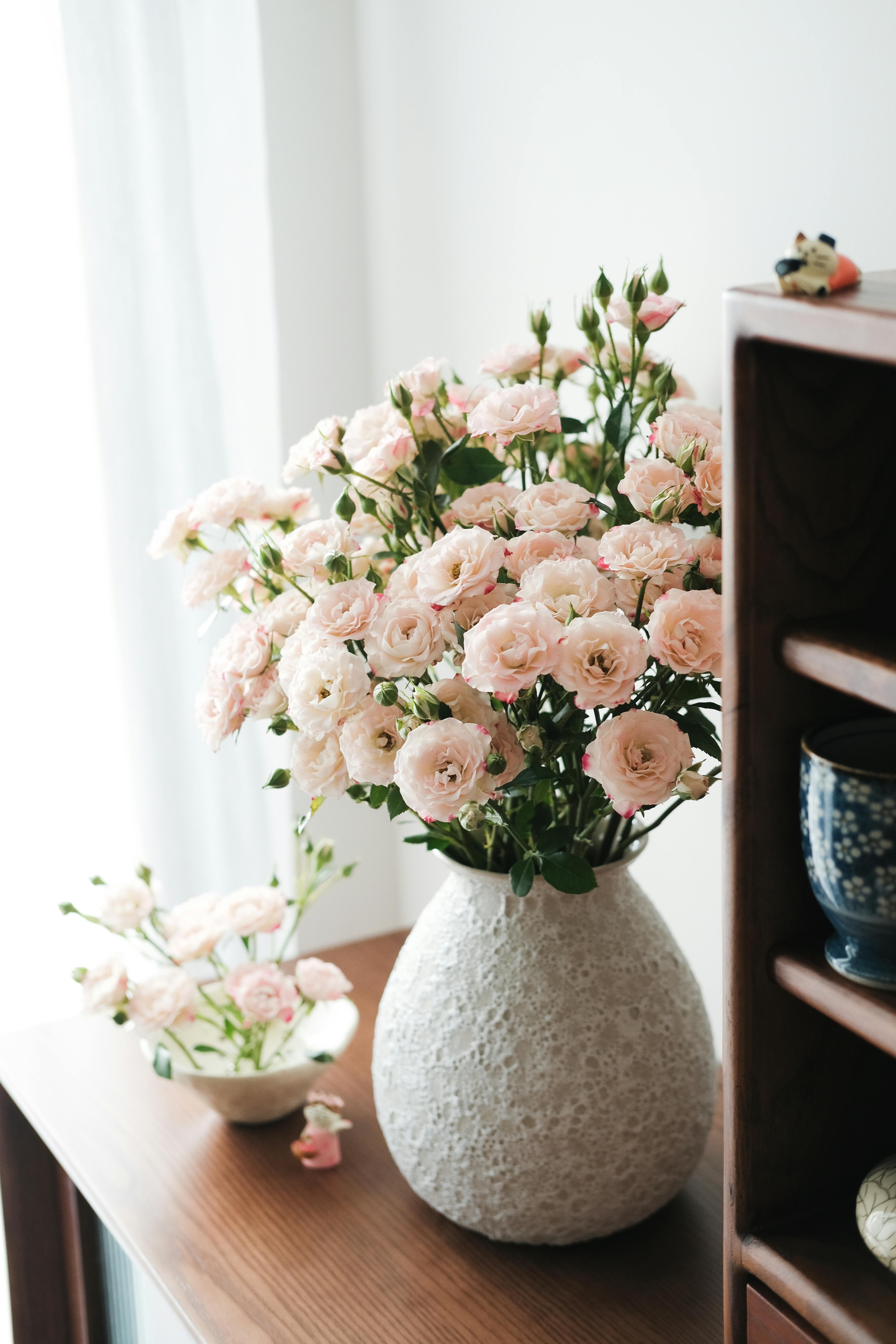 A serene arrangement of pink roses in a textured vase on a wooden table indoors.