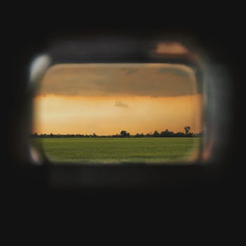 A picturesque landscape of a green field and sunset sky viewed through a unique window frame.