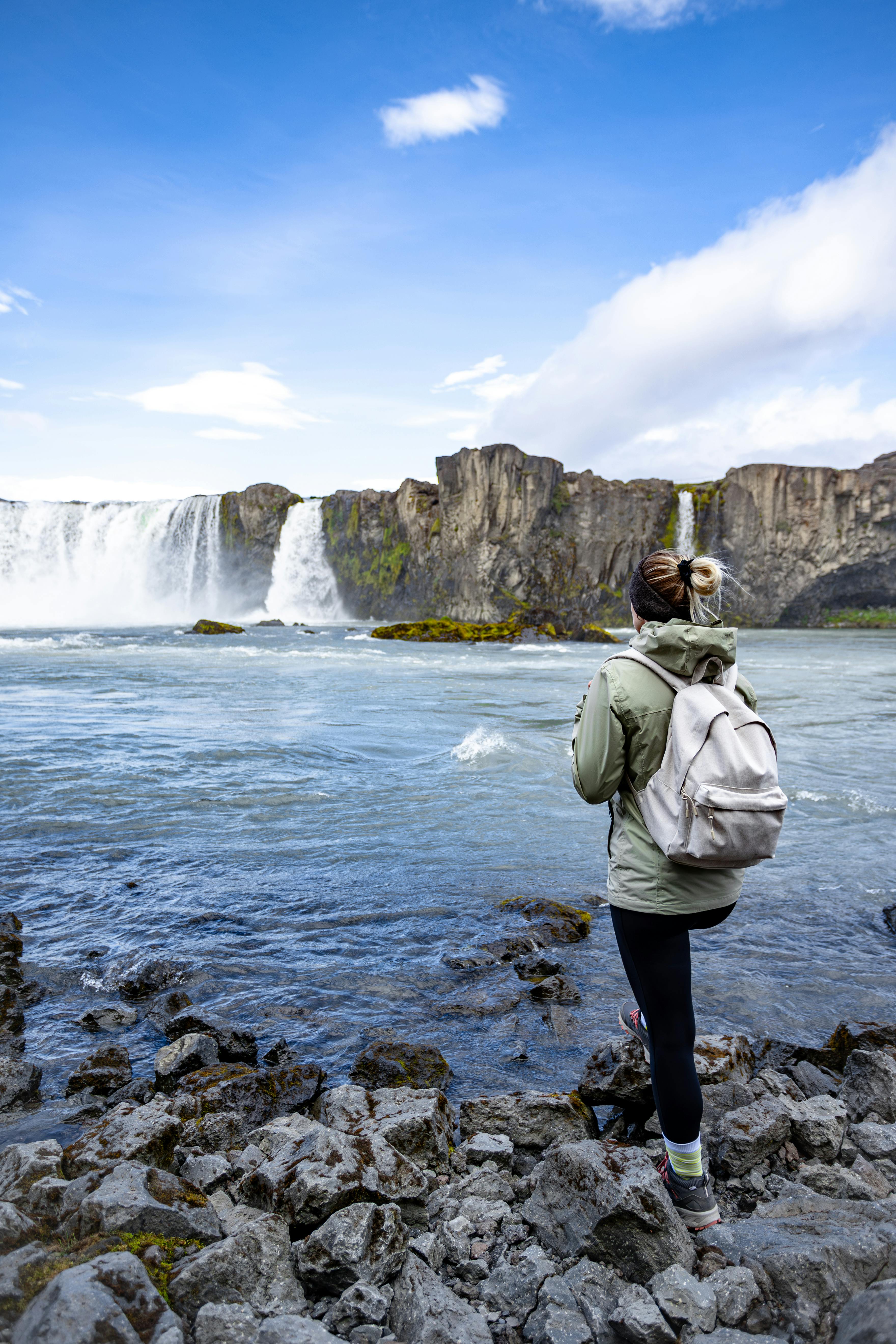 a woman stands on the rocks and looks at the waterfall